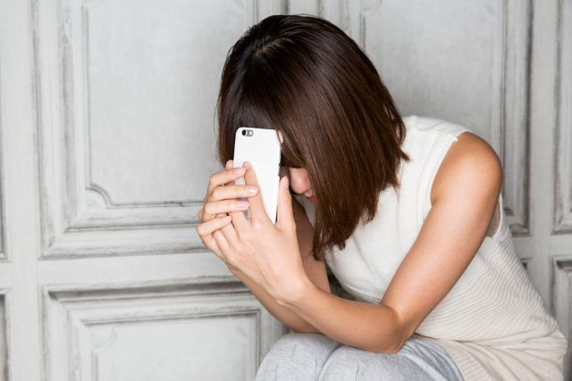 携帯を顔の前にあててうなだれる女性